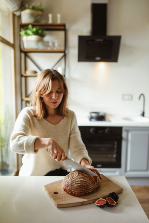 Free A woman slices freshly baked sourdough bread in a cozy kitchen setting, creating a warm and inviting atmosphere. Stock Photo