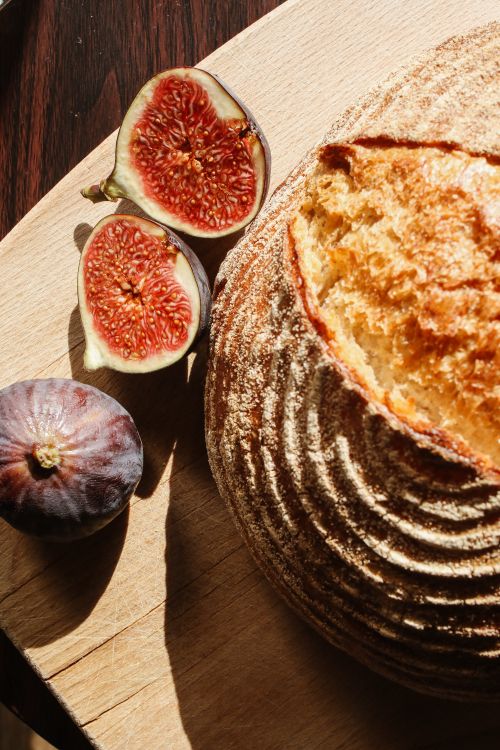 Free Freshly baked sourdough bread with figs displayed on a wooden cutting board in sunlight. Stock Photo