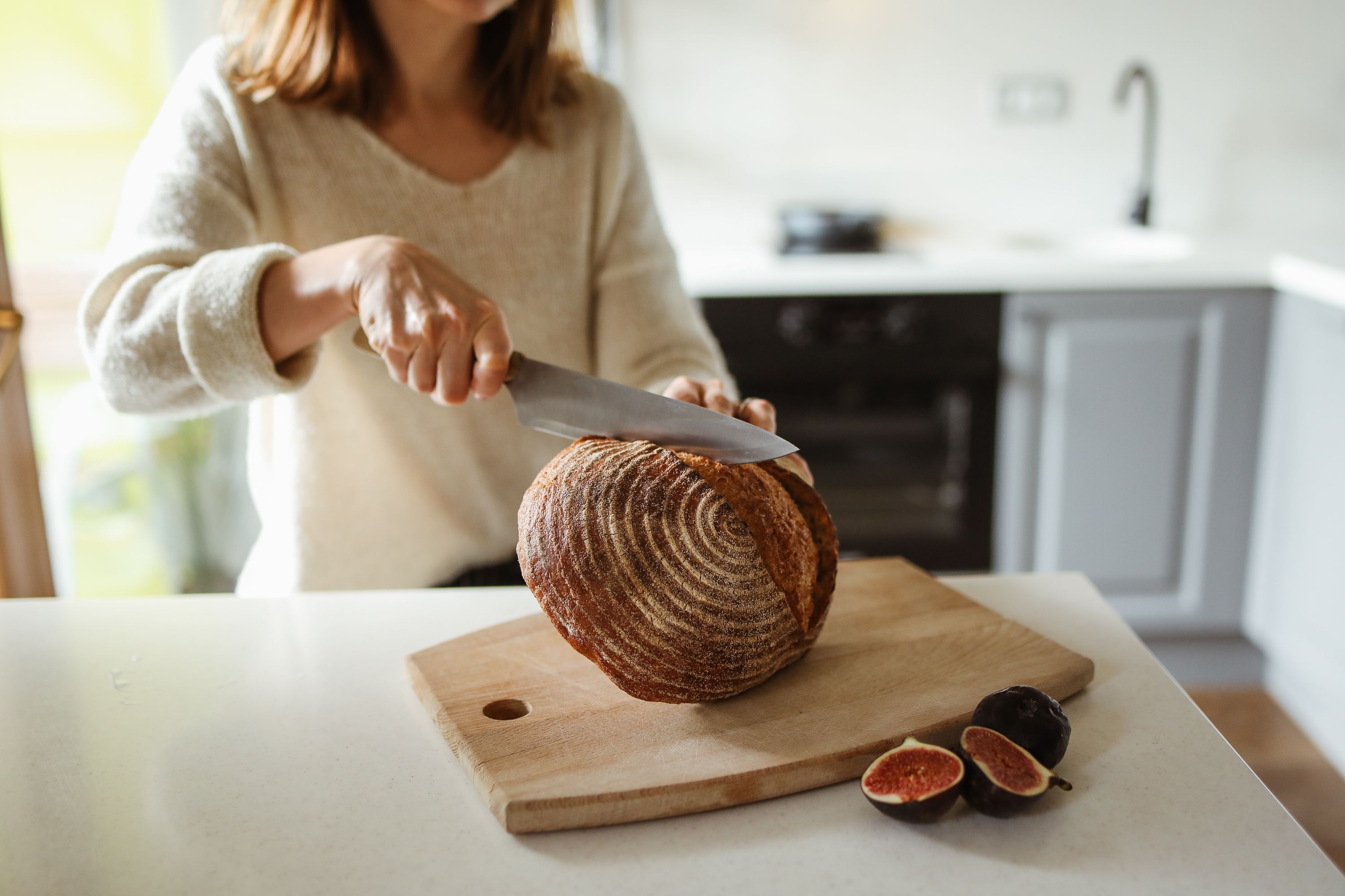 A woman expertly slices artisan bread on a wooden cutting board in a cozy kitchen.