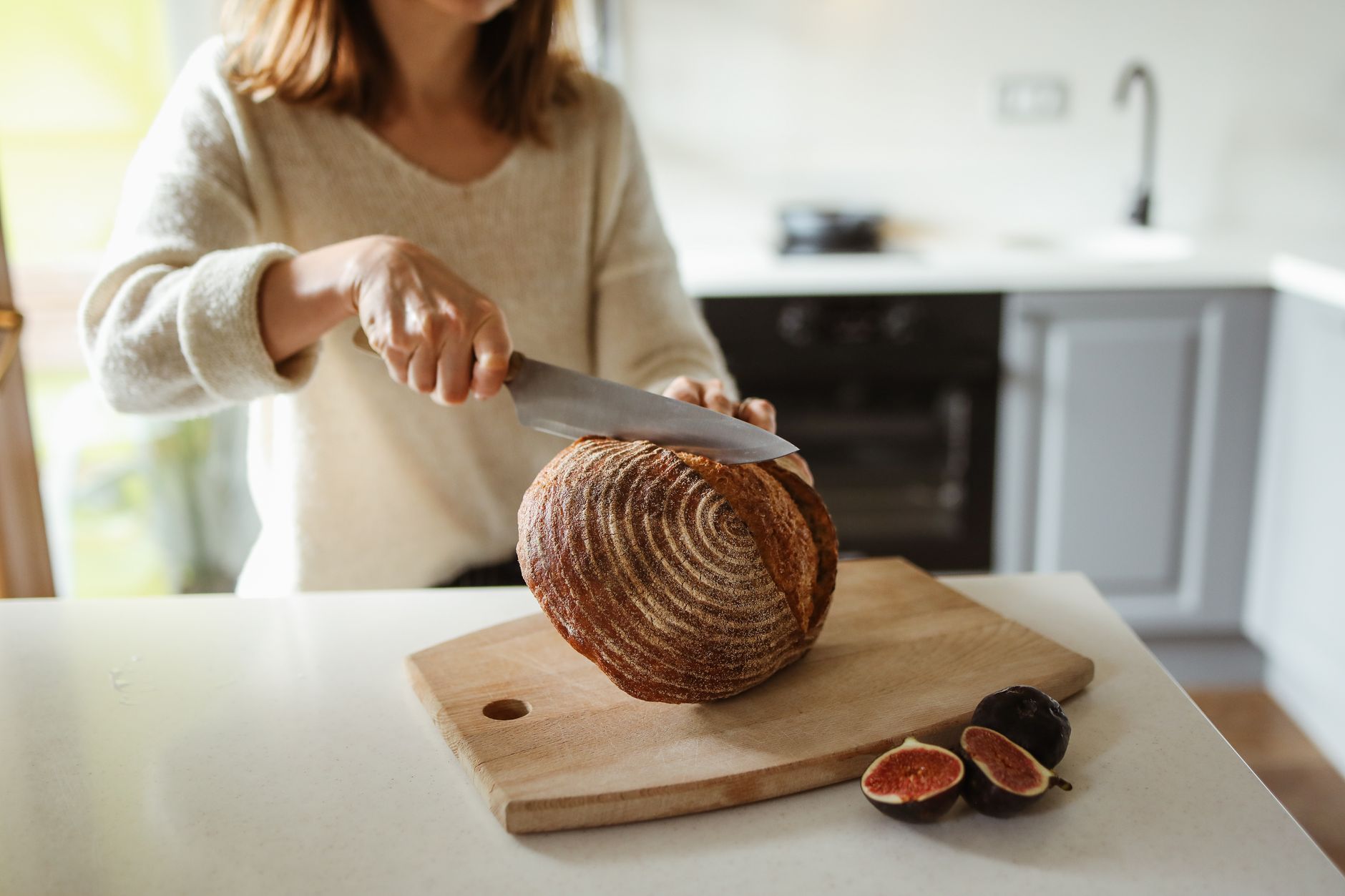 A woman expertly slices artisan bread on a wooden cutting board in a cozy kitchen.