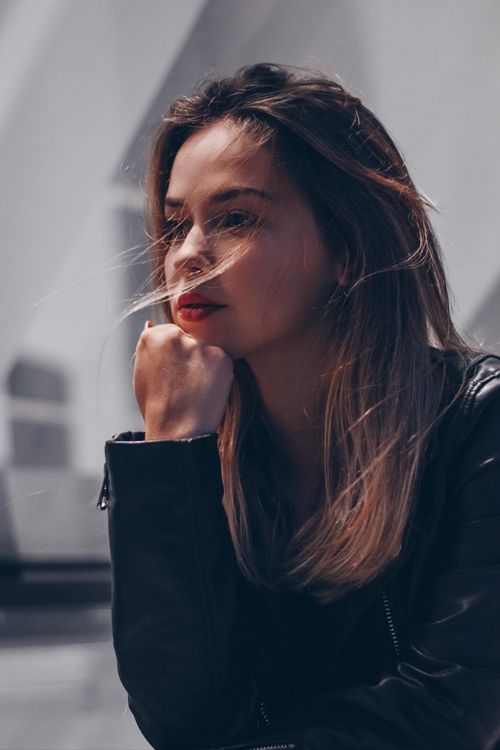 Free Portrait of a woman with long brown hair outdoors, hand on chin, looking thoughtful. Stock Photo