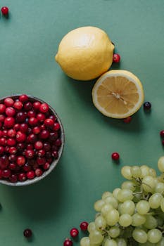 Colorful still life of fresh lemons, cranberries, and grapes on a green background.
