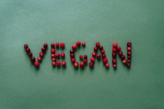 Cranberries arranged to spell 'vegan' on a vibrant green background, top-down view.