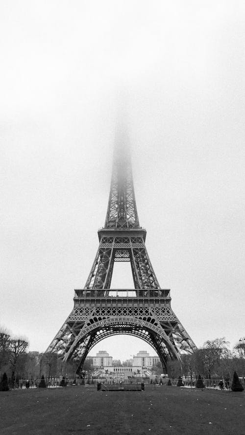 Black and white exterior of majestic famous Eiffel Tower with peak in dense fog