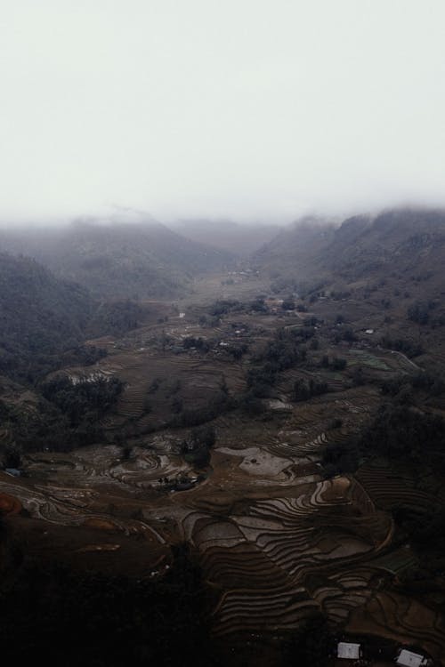 Drone view scenery of spacious green highland valley near small settlement on foggy weather