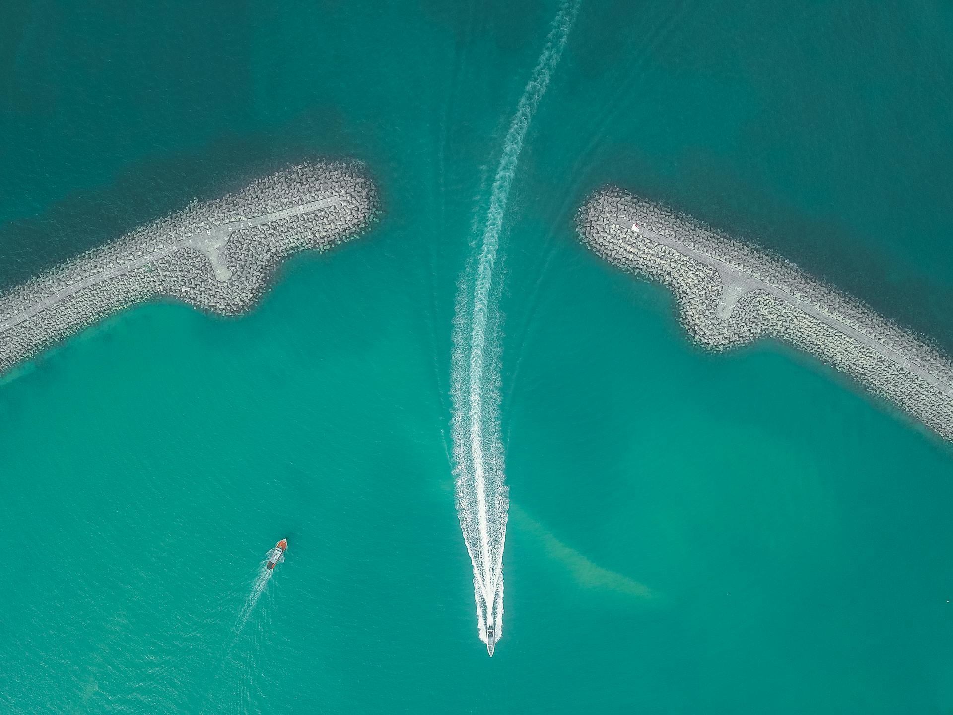 Aerial view of colorful azure calm sea with boats sailing near rocky embankment