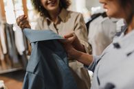 女士们在一家现代精品店里仔细审视一件蓝色服装，强调购物体验