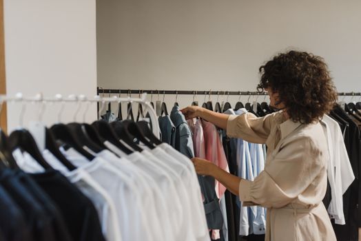 一名妇女在精品店里浏览衣服，从架子上挑选各种时尚衬衫