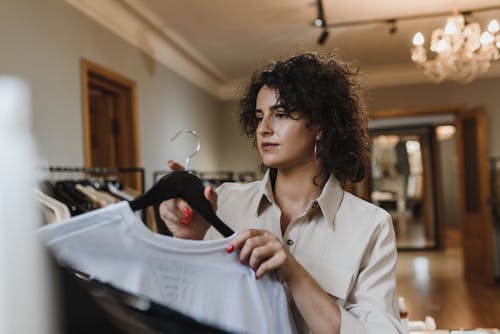 Woman in Beige Long Sleeve Shirt Holding Clothing Hanger