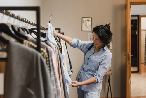 Free A woman examines clothes on a rack in a stylish boutique, considering her shopping options. Stock Photo