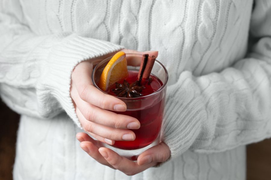 Hands cradling a glass of vin chaud with orange and spices