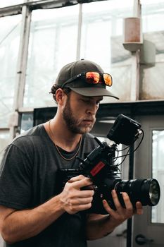 Male videographer focused on filming with a professional camera indoors, wearing sunglasses on cap.