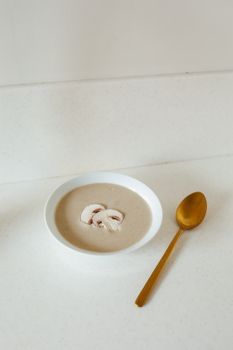 Creamy mushroom soup served in a white bowl with golden spoon on white surface.