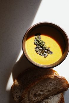 A cozy flatlay of pumpkin soup garnished with seeds and served with slices of bread, perfect for autumn.