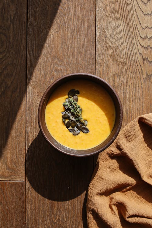 Brown and Black Ceramic Bowl on Brown Wooden Table with Pumpkin Soup