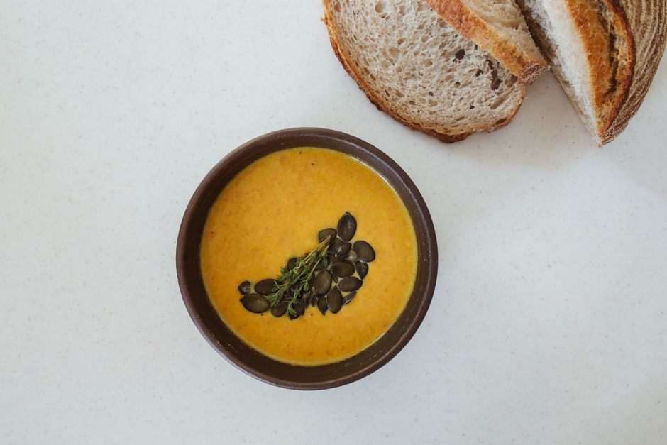 Top-down view of a bowl of pumpkin soup garnished with seeds and thyme, served with bread.