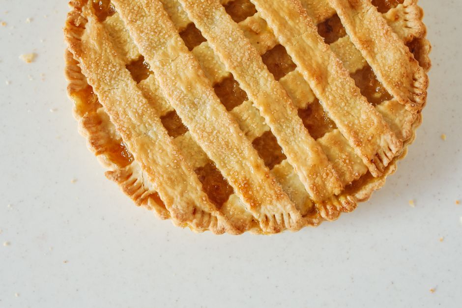A close-up top view of a freshly baked lattice-top lemon pie on a light background.