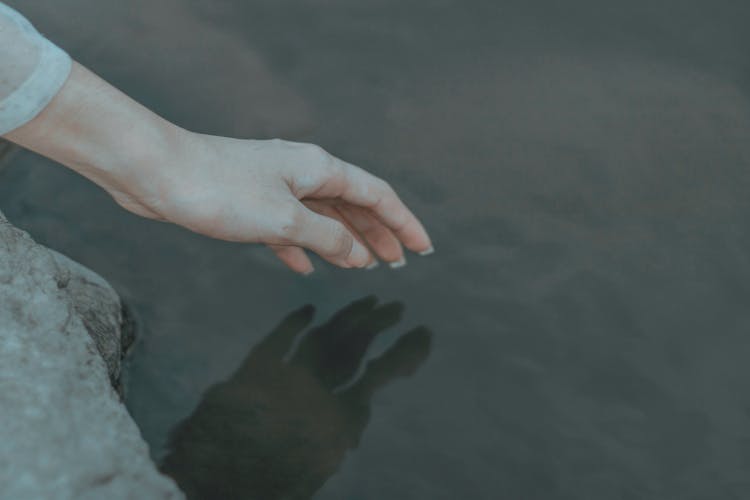 Faceless Lady On Stone Surface Touching Lake With Hand