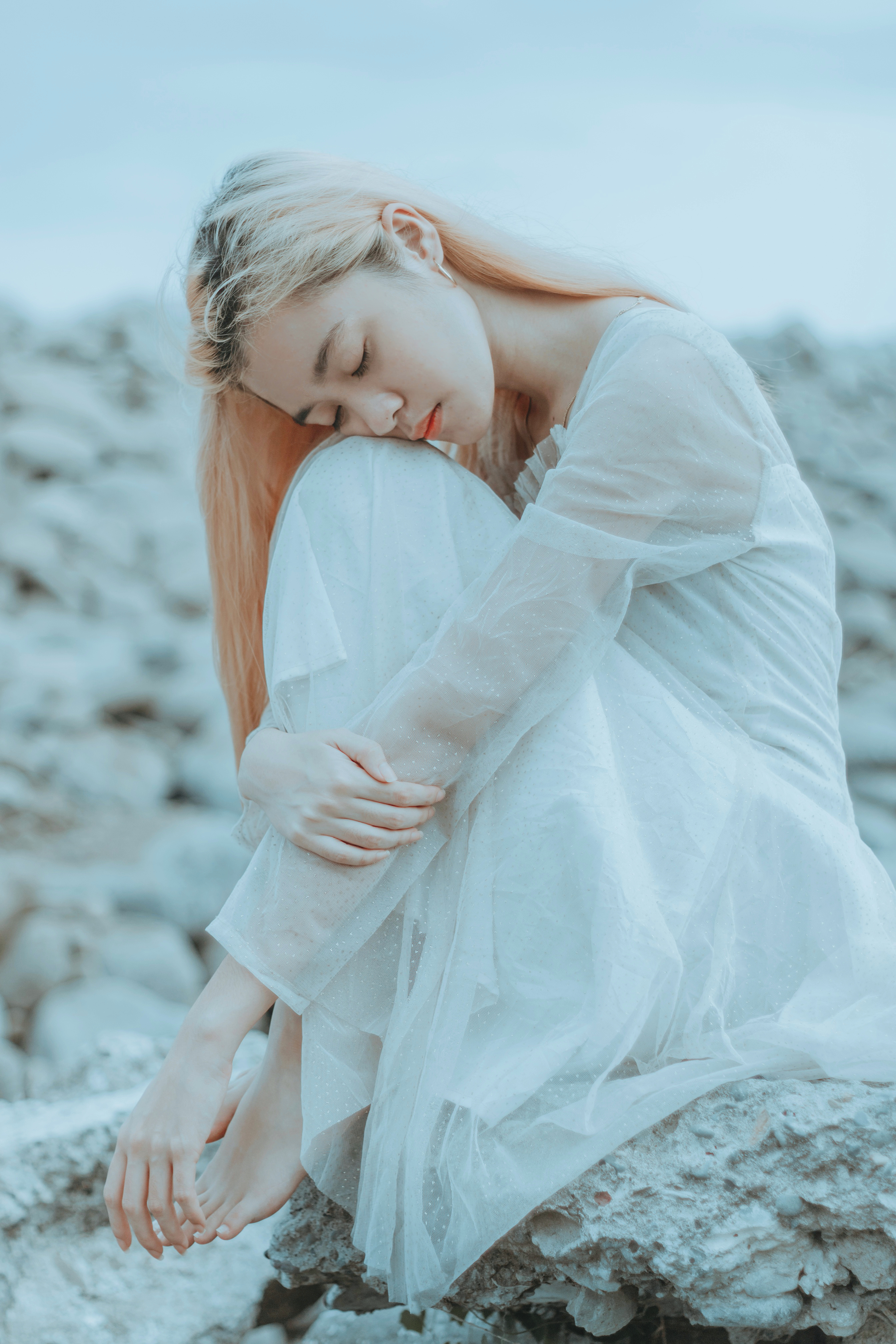 一位身着白裙的年轻女子静坐于岩石之上，画面宁静，尽显平静与优雅