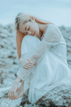 一位身着白裙的年轻女子静坐于岩石之上，画面宁静，尽显平静与优雅