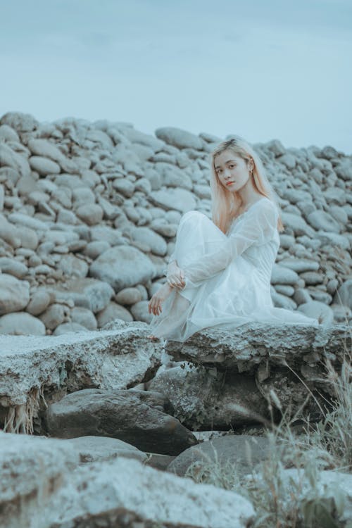 Thoughtful Asian lady in dress sitting on rocky surface