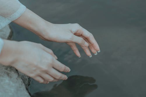 Free Crop anonymous female in elegant clothes reaching hands to calm water in daytime Stock Photo