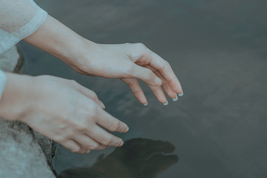 白天，一位身着优雅衣装的匿名女子伸手探向平静的水面