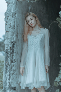 一名身穿白色连衣裙的女子若有所思地靠在户外饱经风霜的墙壁上摆出姿势