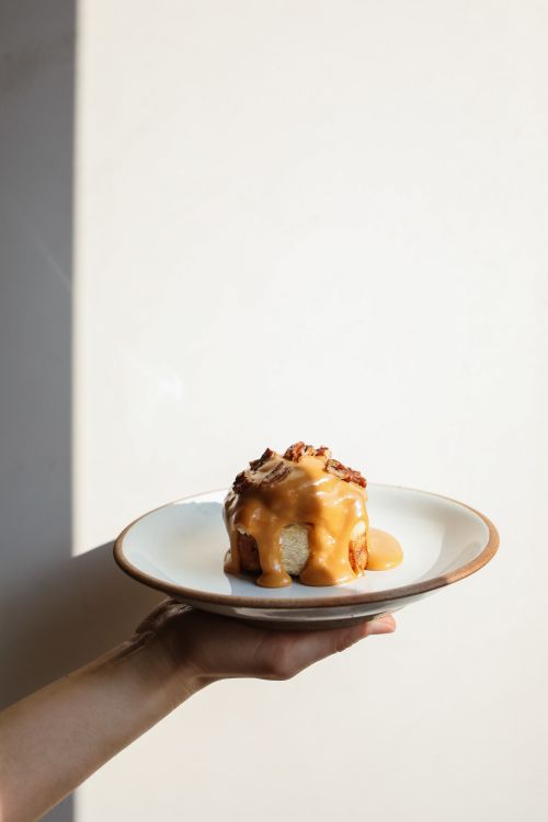 Free A hand holds a plate with a cinnamon roll drizzled in caramel sauce, perfect for food photography. Stock Photo