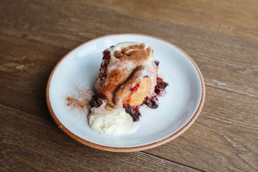 Delicious cinnamon roll topped with icing and red berries on a plate.