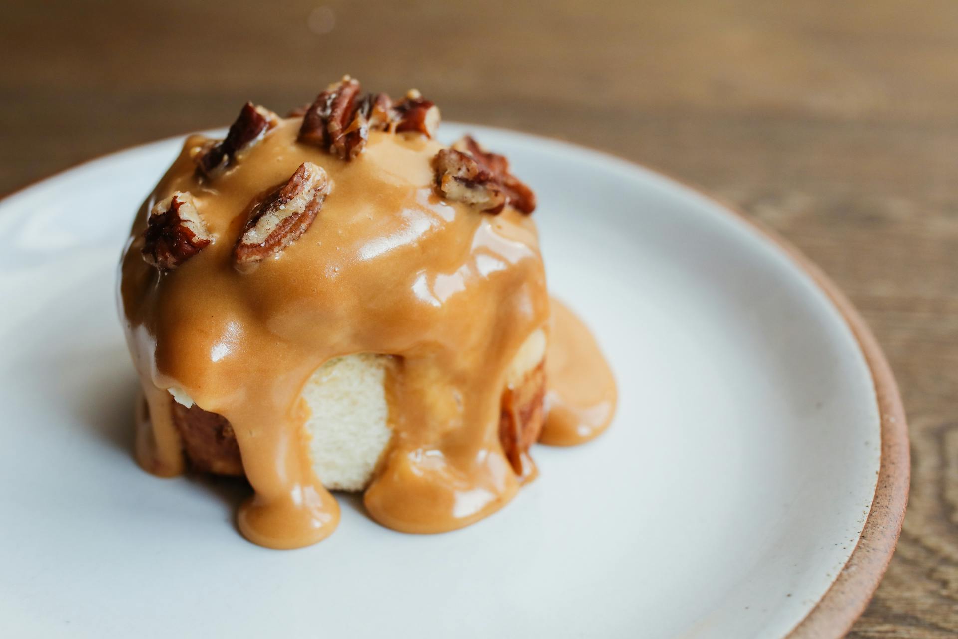 Close-up of a sticky bun with caramel glaze and pecans on a plate.