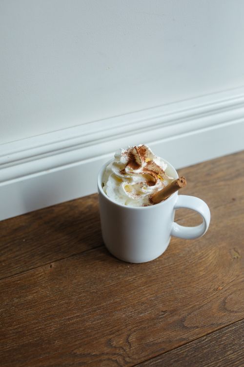 Free White mug of hot chocolate topped with whipped cream and cinnamon stick on a wooden floor. Stock Photo