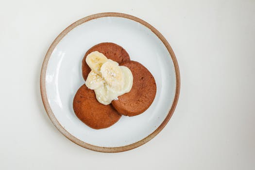 Top view of pancakes with banana slices and cream on a ceramic plate.