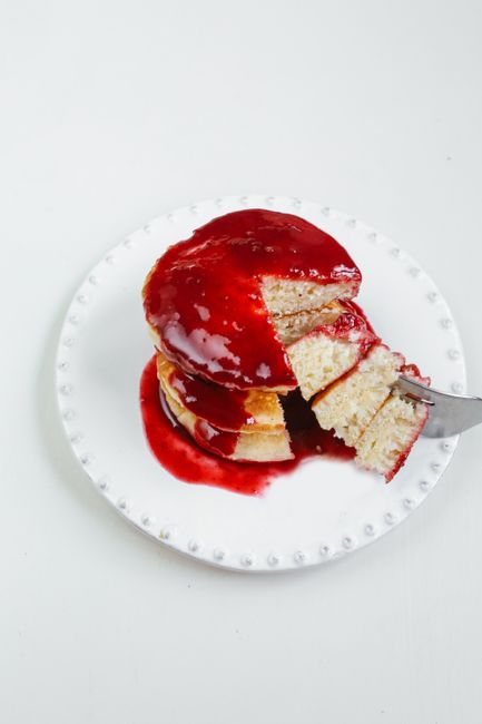 Delicious pancakes topped with strawberry syrup on a white plate, creating a mouthwatering treat.