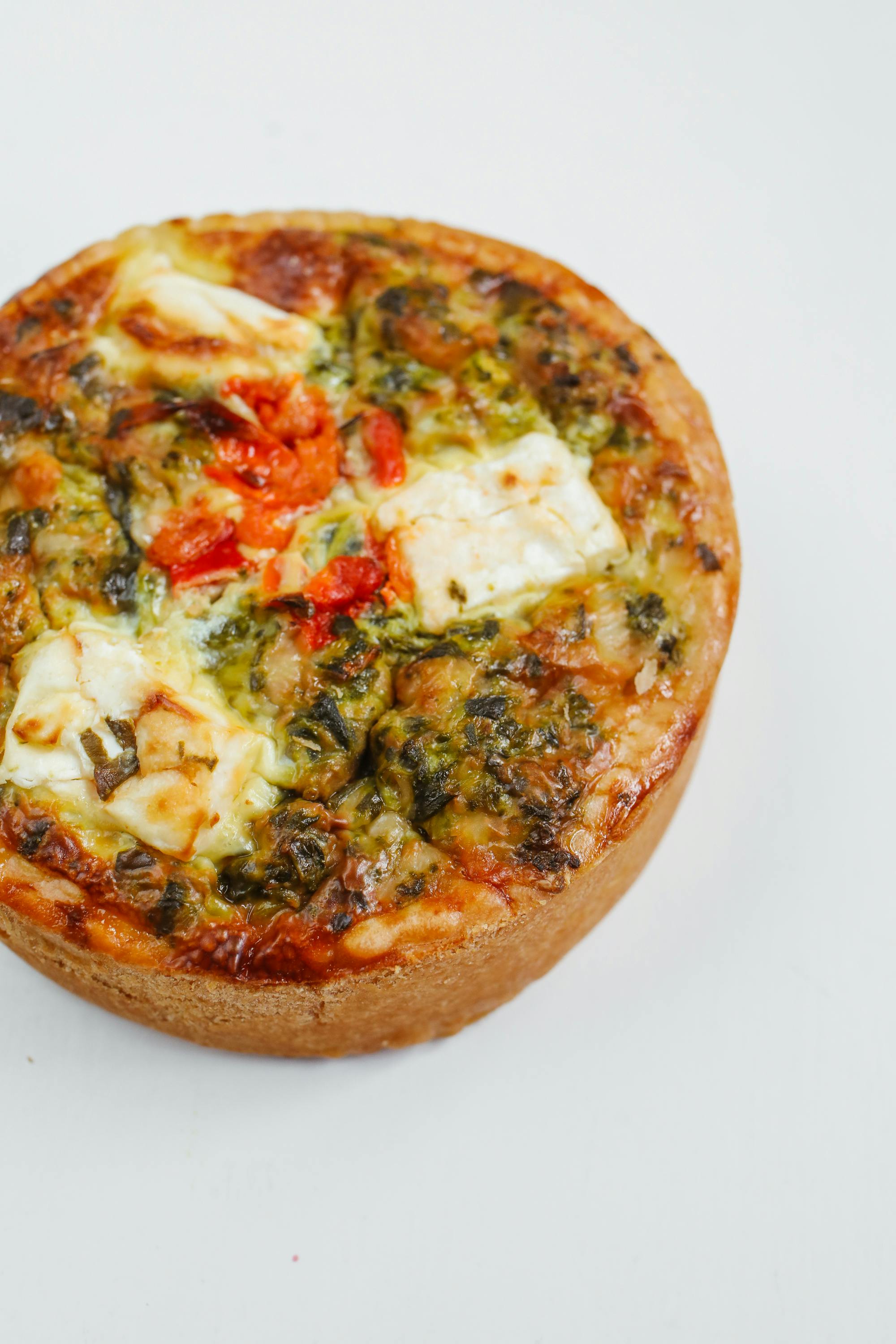 Polina Tankilevitch - Freshly baked spinach and cheese quiche on a clean white background, perfect for food photography.