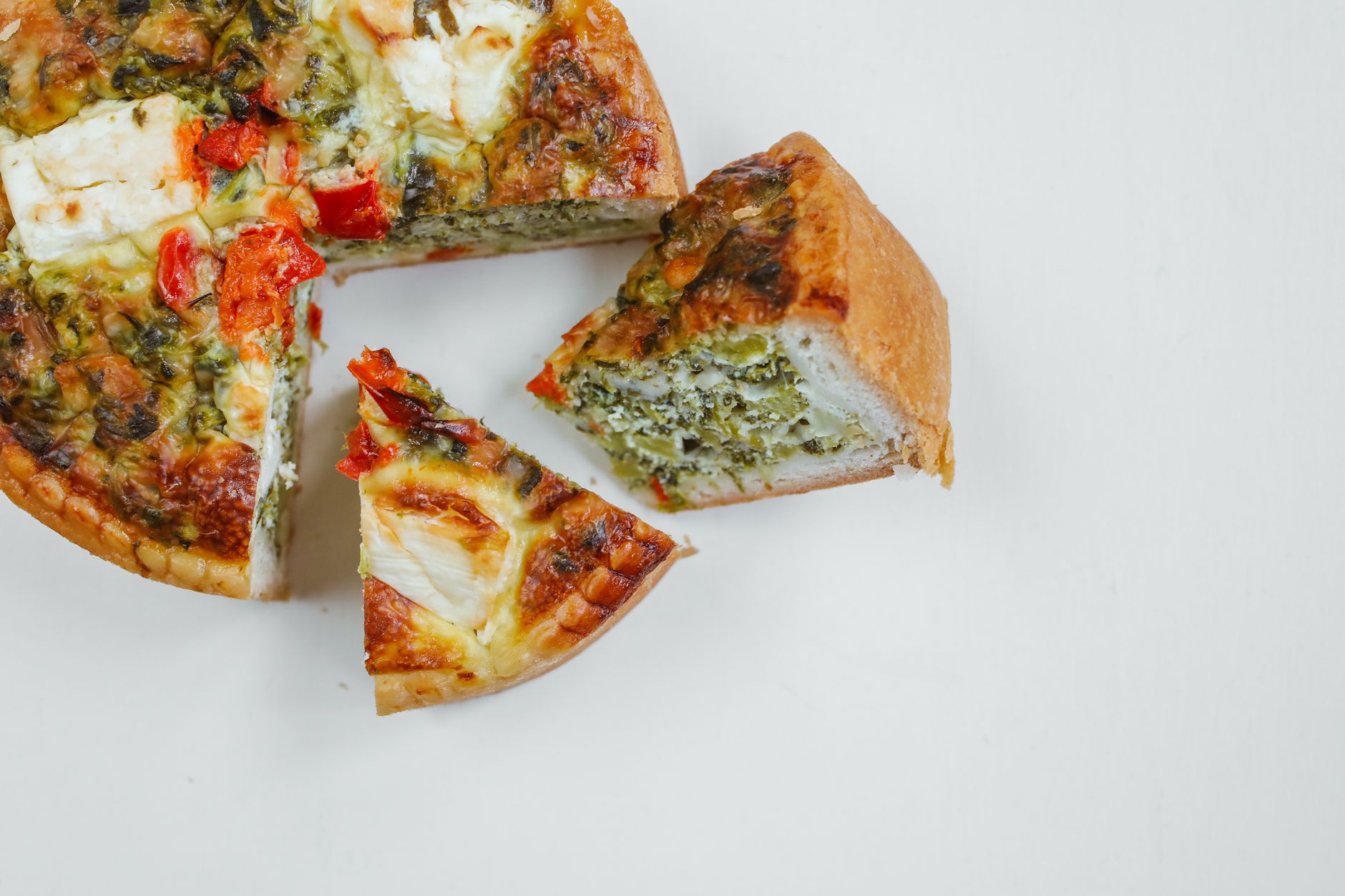 Slice of ham and spinach quiche on a plate with fresh herbs