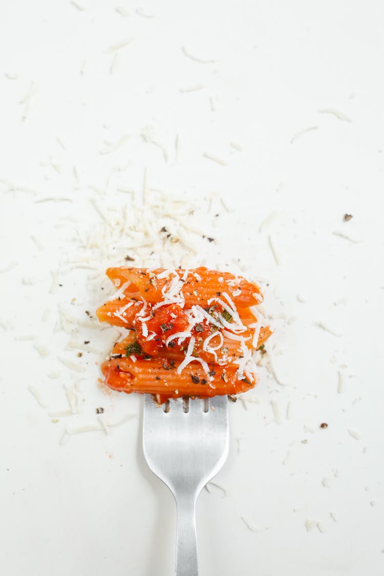 A Delicious Penne Pasta Dashed With Grated Cheese And Pepper On Fork