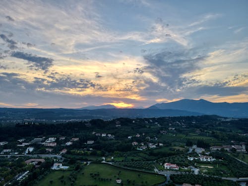 Amazing drone view of residential houses located in green valley under cloudy sunset sky in mountainous countryside