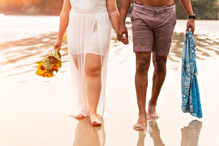 A Couple Walking On A Wet Shore Holding Hands