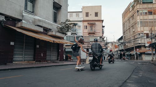 A Woman Skateboarding on the Road Holding to a Motorcycle