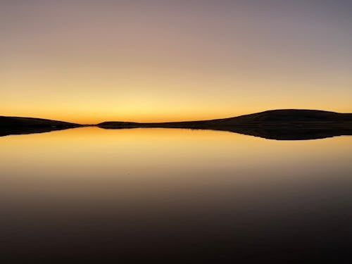 Calm and Still Lake at Sunset and Silhouette of Mountains Reflecting in Water 