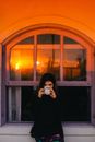 Woman Drinking Coffee while Sitting on a Windowsill Outdoors at Sunset 