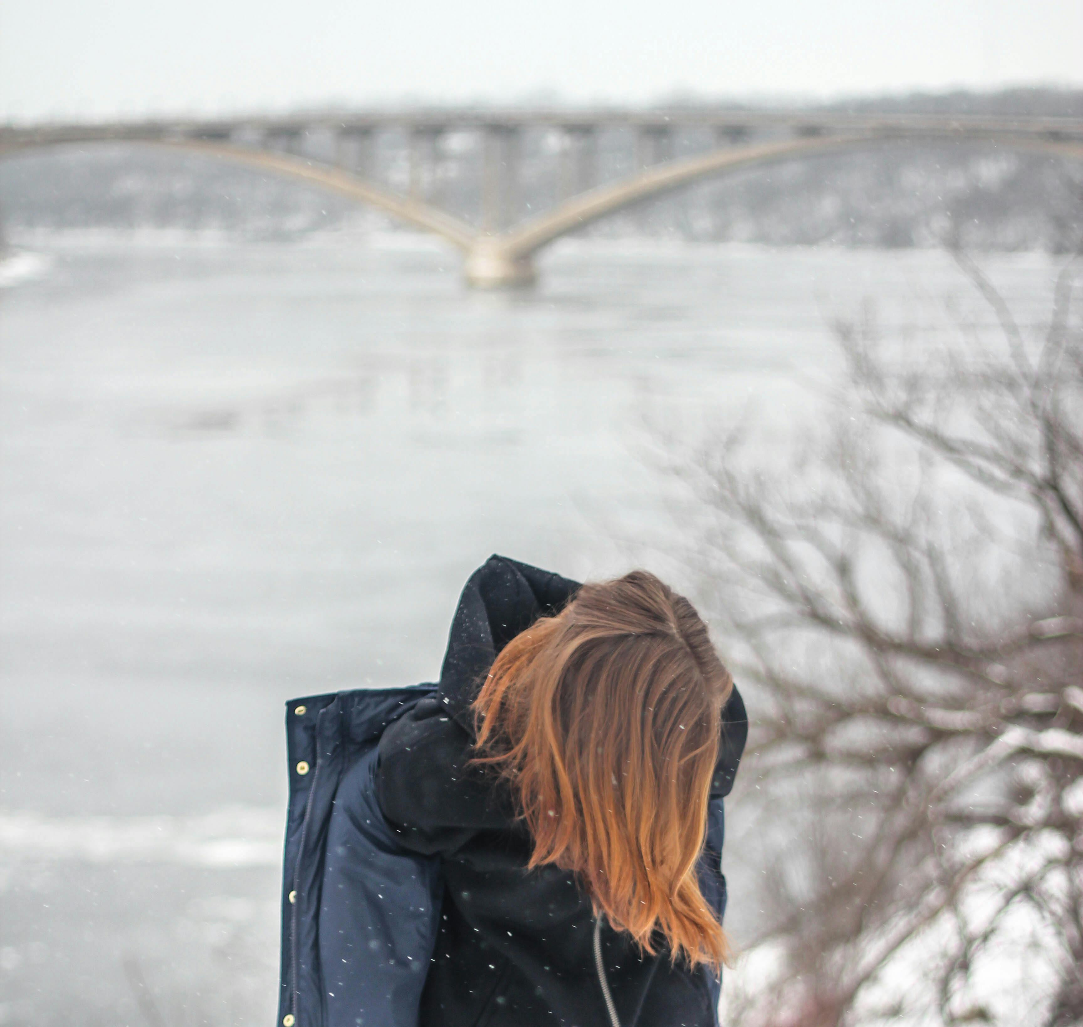 一个女人在冬天沿着冰冻的河流和桥梁行走，捕捉孤独和寒冷的天气