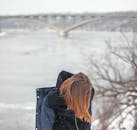 一个女人在冬天沿着冰冻的河流和桥梁行走，捕捉孤独和寒冷的天气