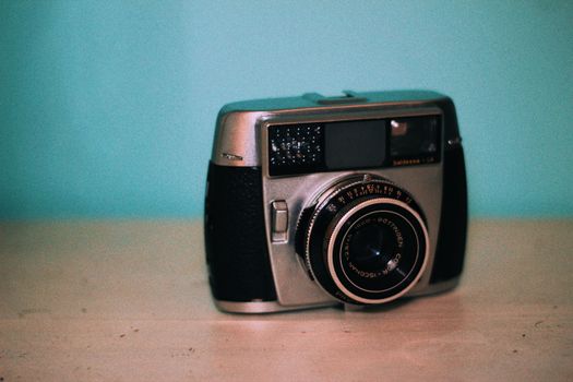 Vintage photo camera with shiny lens and buttons on wooden table near wall
