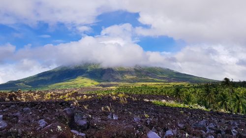 Free Majestic Mayon Volcano shrouded in clouds, surrounded by lush greenery and volcanic soil. Stock Photo