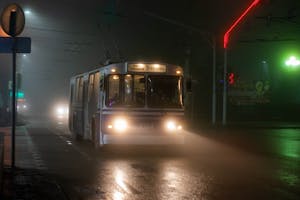 Old trolleybus driving along wet asphalt road in small city at foggy night