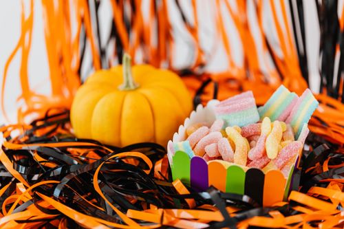 Free Colorful candies in a vibrant box next to a small pumpkin surrounded by Halloween-themed decorations. Stock Photo