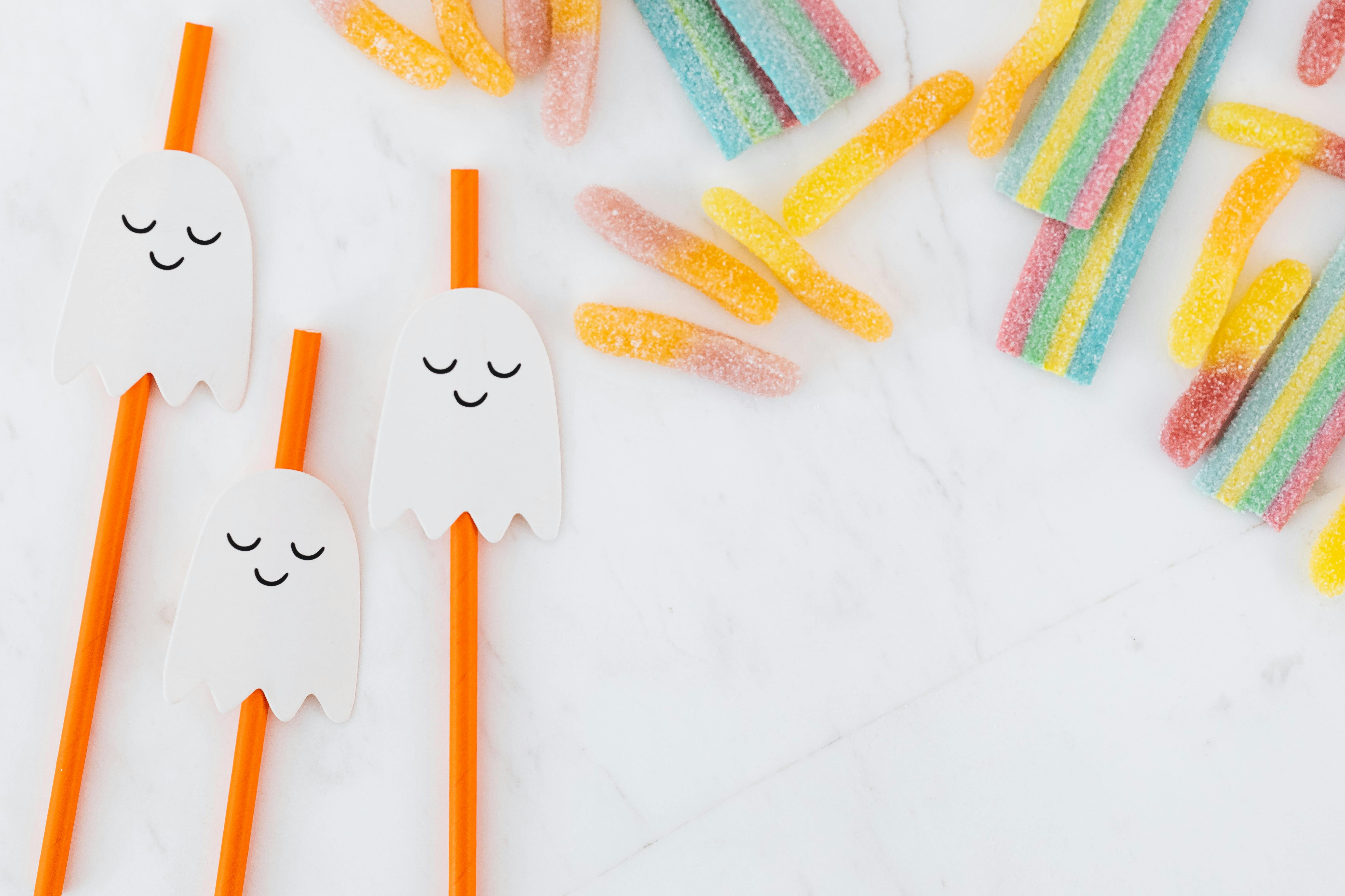 大理石表面上的彩色糖果和鬼魂主题吸管的顶视图，非常适合节日派对