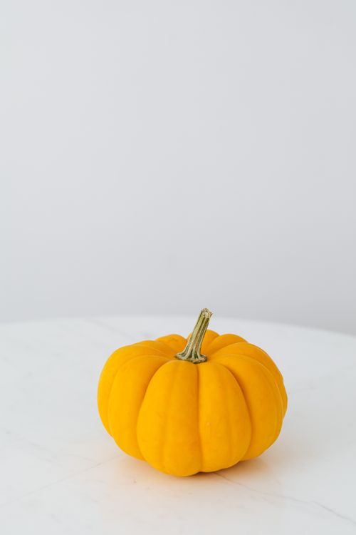Free Bright and fresh yellow pumpkin placed on a white table, ideal for fall themes. Stock Photo